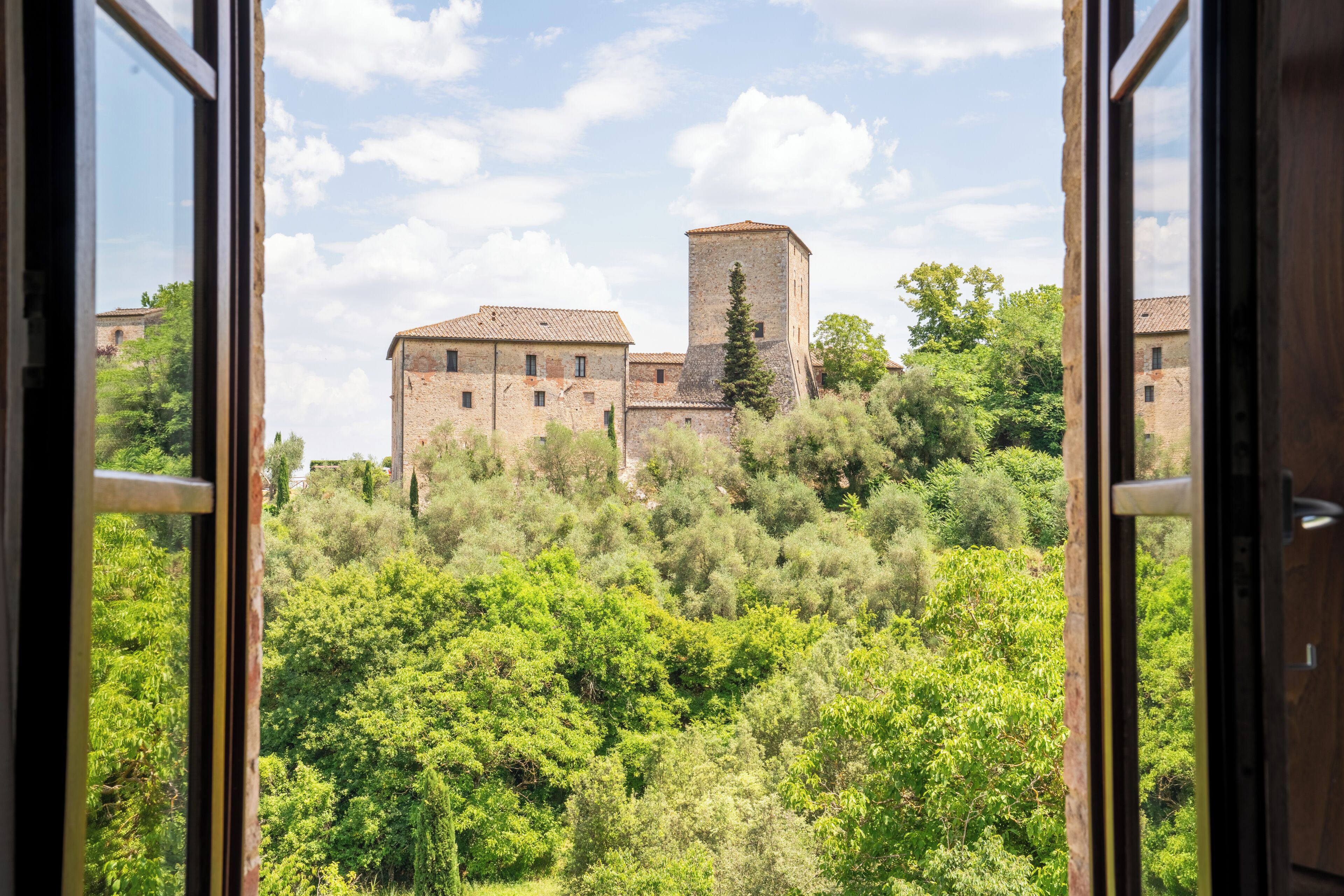 A view through a window of a historic building with a tower, surrounded by lush greenery.