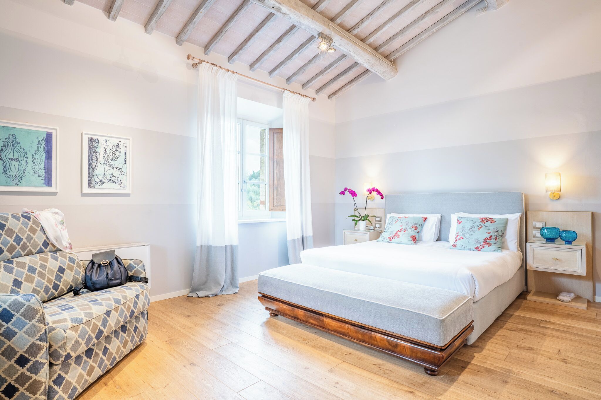 A bedroom with a bed, a sofa, a nightstand, and a window with curtains.