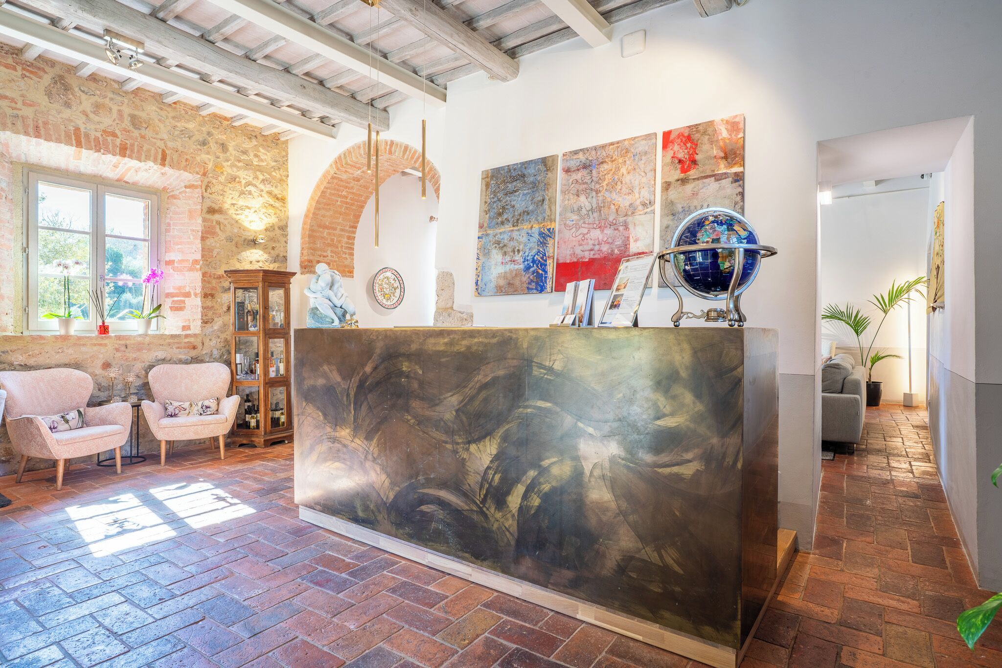 A reception area with a stone wall, a large abstract painting, a globe, and a brick floor.