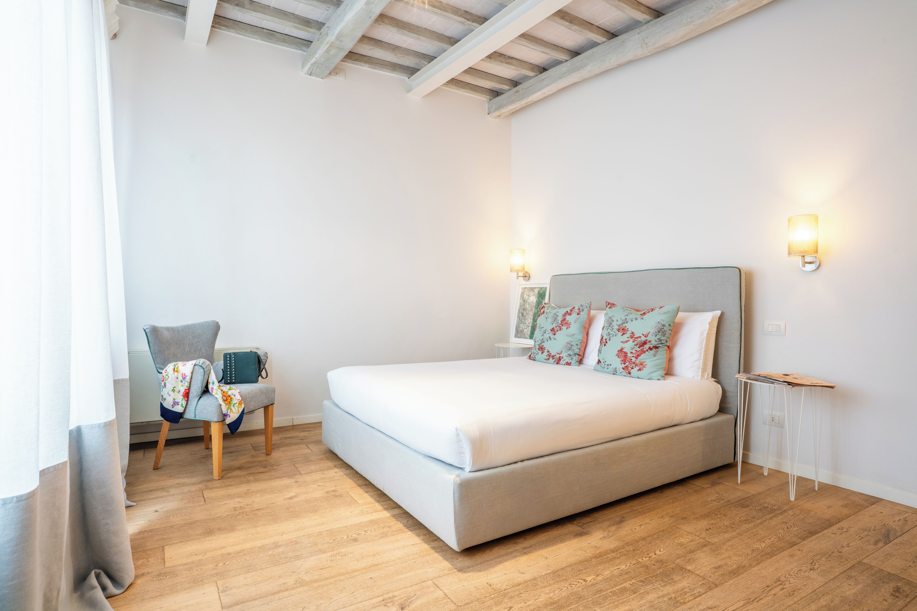 Un dormitorio con una cama, una silla, una mesita y dos lámparas de pared.