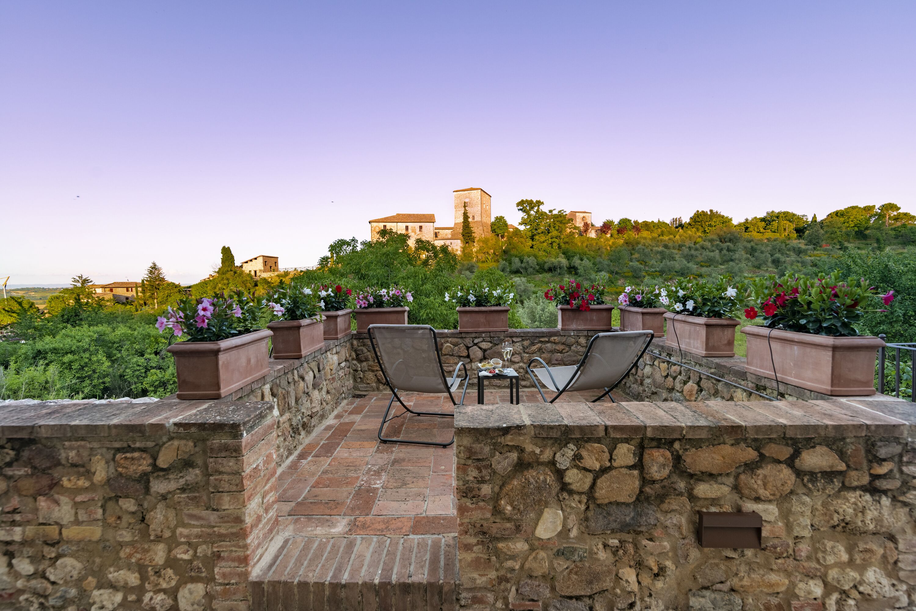 An outdoor patio with stone walls, two chairs, a table, and potted plants.