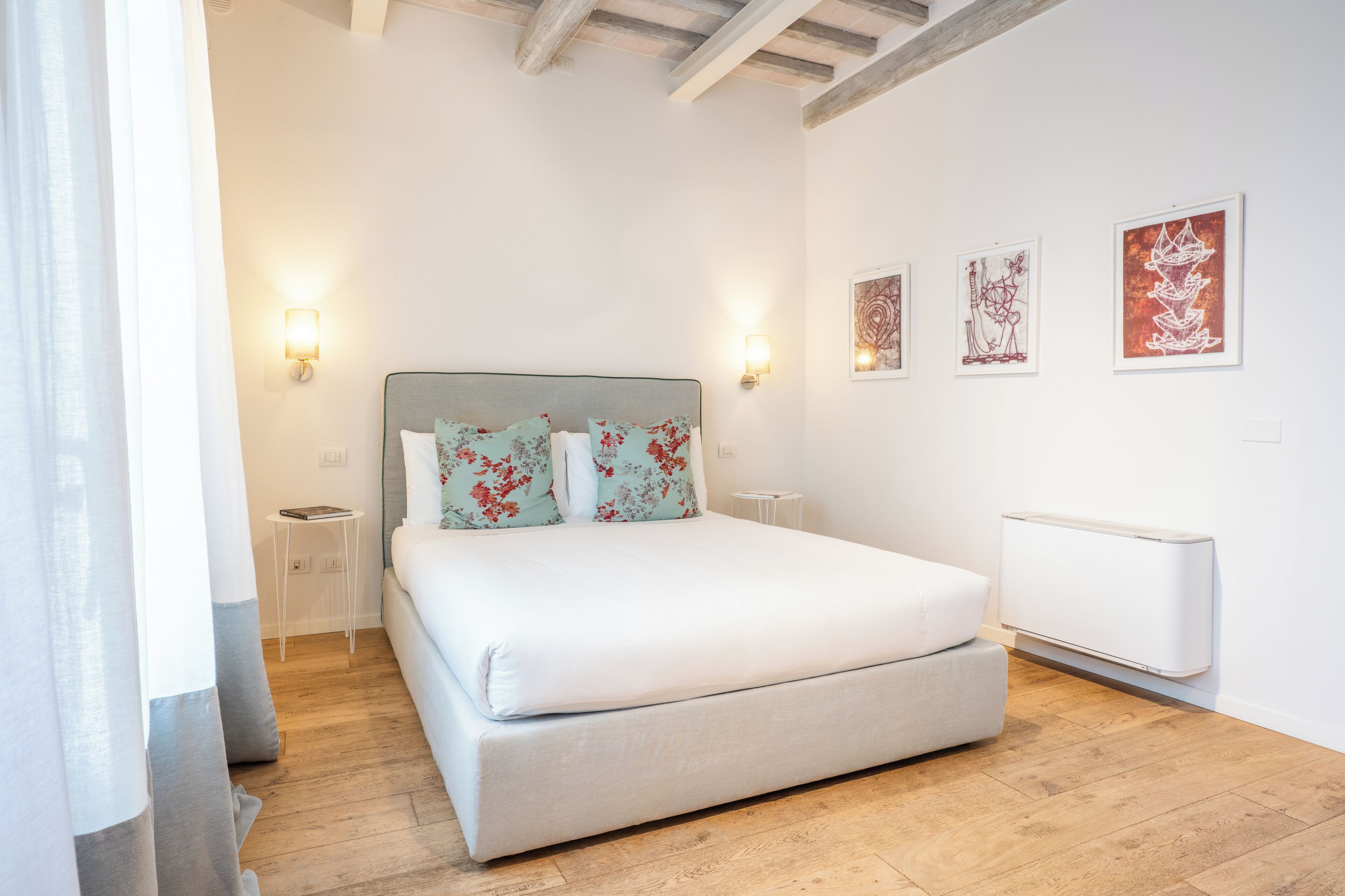 A bedroom with a bed, bedside tables, wall-mounted artwork, and a radiator.