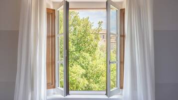 A window with white curtains, a wooden frame, and a view of a tree and building outside.