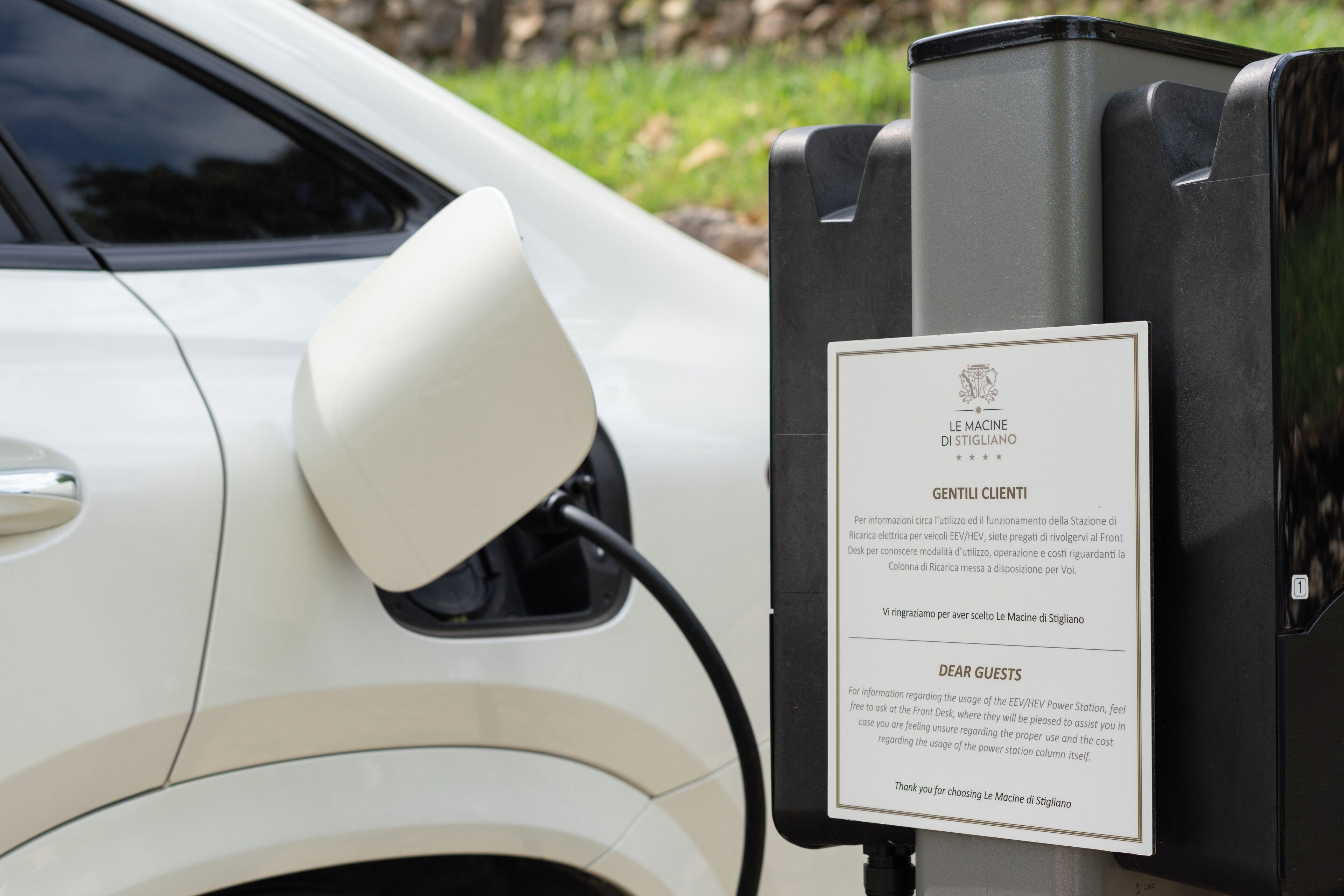 A charging station with a sign for Le Macine di Stigliano, indicating it is an EV charging station.