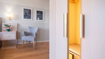 Une pièce avec un plancher en bois, un mur blanc, une chaise, une table de chevet avec une lampe et des tableaux encadrés.