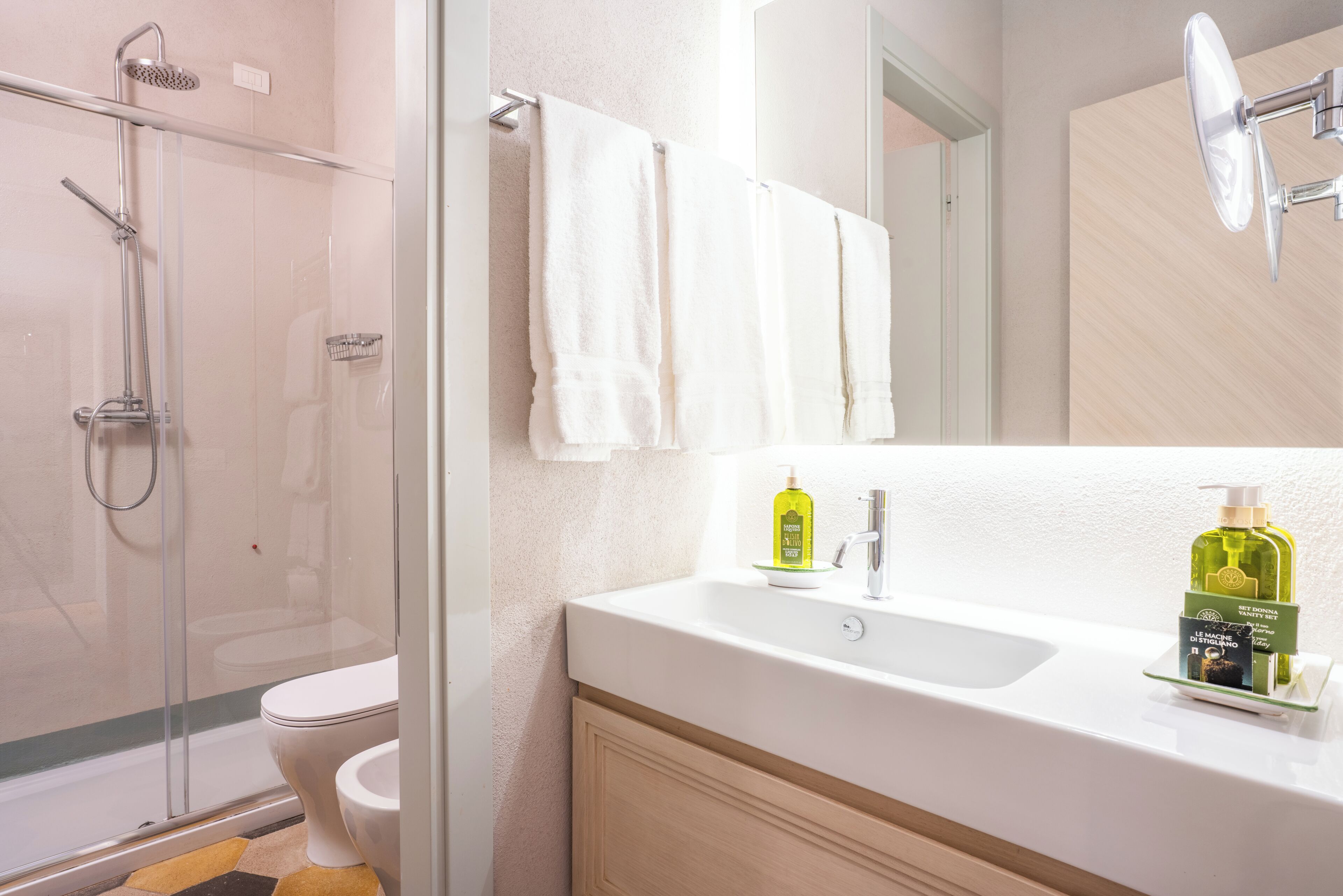 A bathroom with a glass shower enclosure, a toilet, a sink with toiletries, and a mirror.