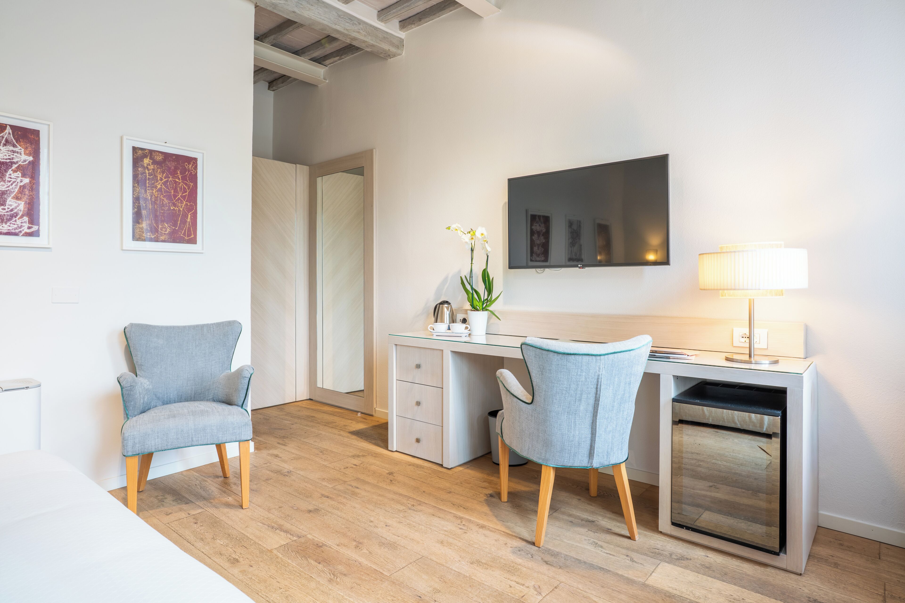 A modern room with a desk, two chairs, a mirror, and artwork on the wall.