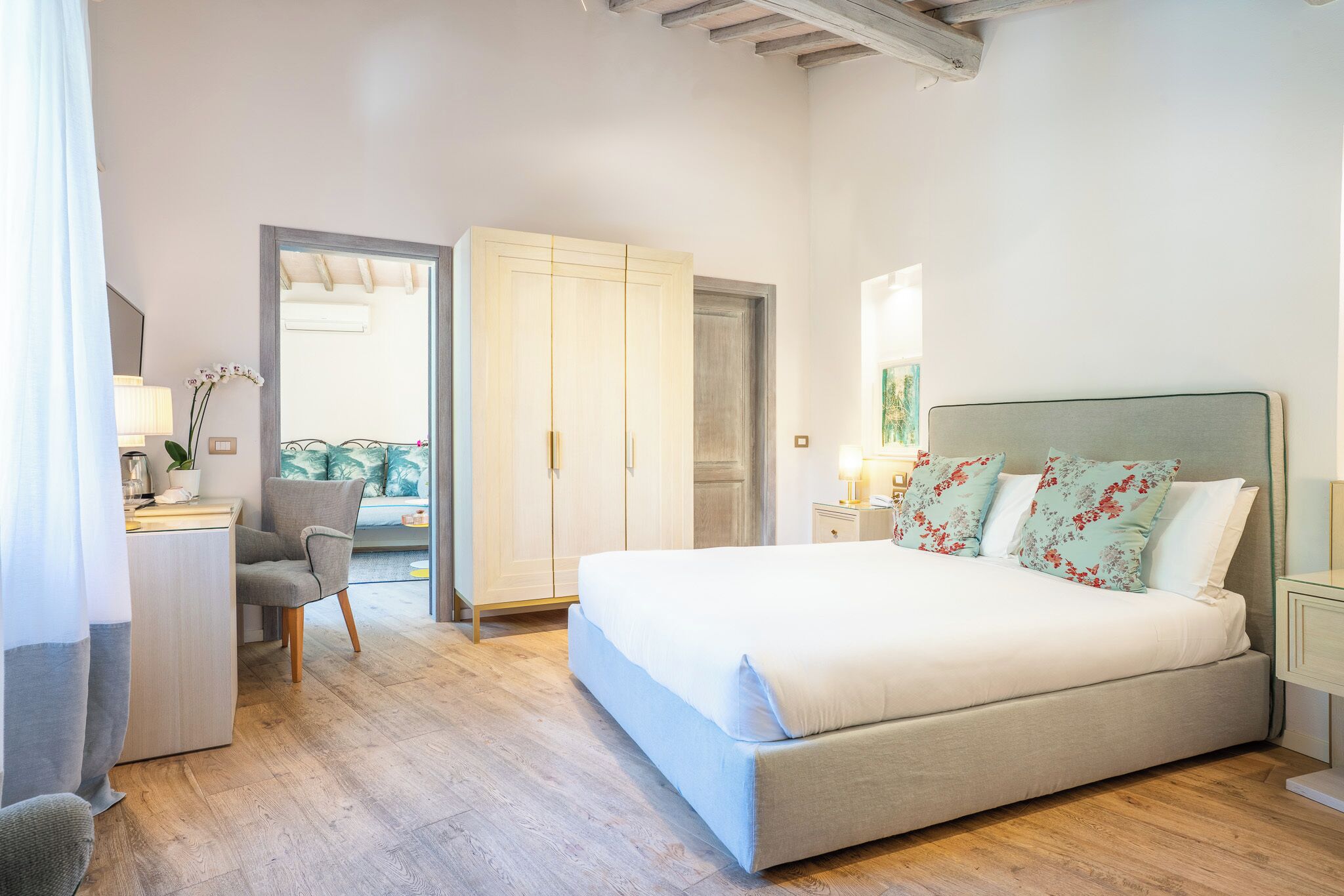 A bedroom with a large bed, a desk with a chair, a wardrobe, and a nightstand with a lamp.