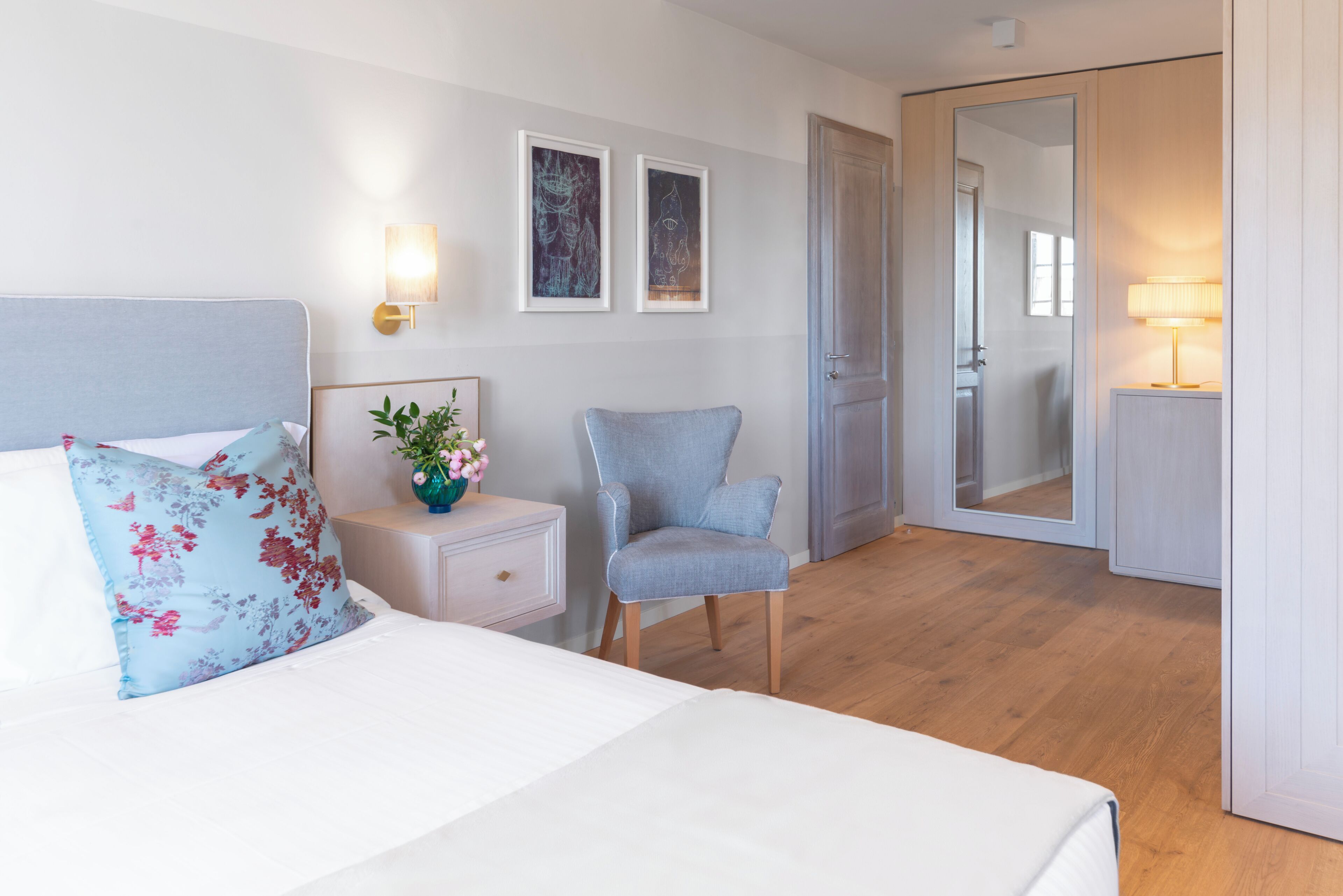 Una habitación de hotel con cama, una silla, mesita de noche, espejo y decoración en la pared.