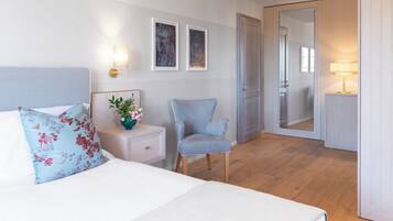 Una habitación de hotel con cama, una silla, mesita de noche, espejo y decoración en la pared.
