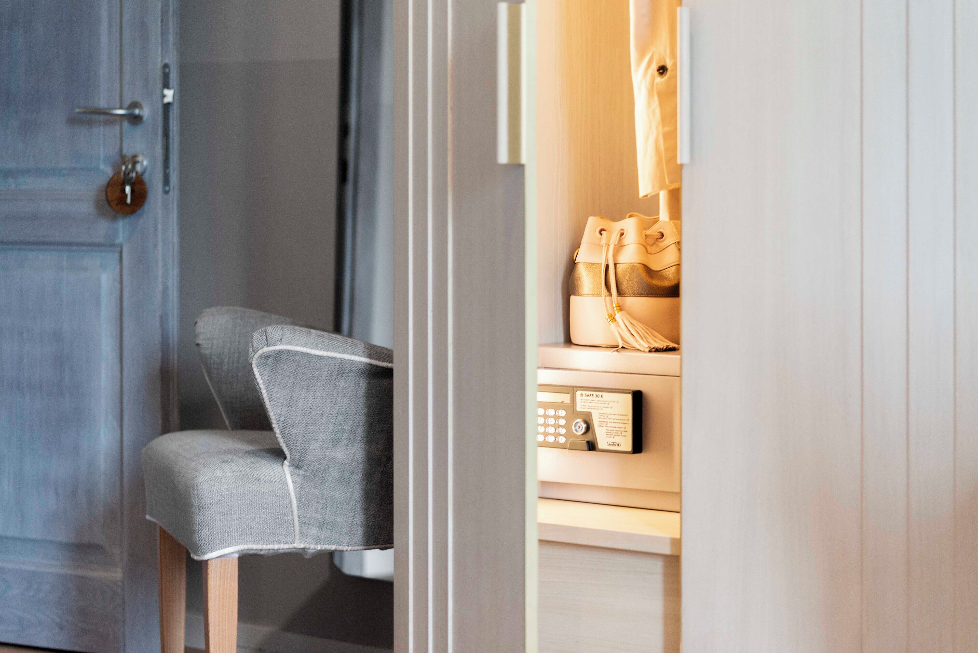 Una habitación con una puerta de madera, un sillón tapizado en gris y un armario de madera con un panel de control.