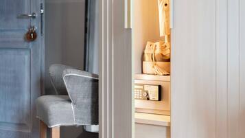 Una habitación con una puerta de madera, un sillón tapizado en gris y un armario de madera con un panel de control.