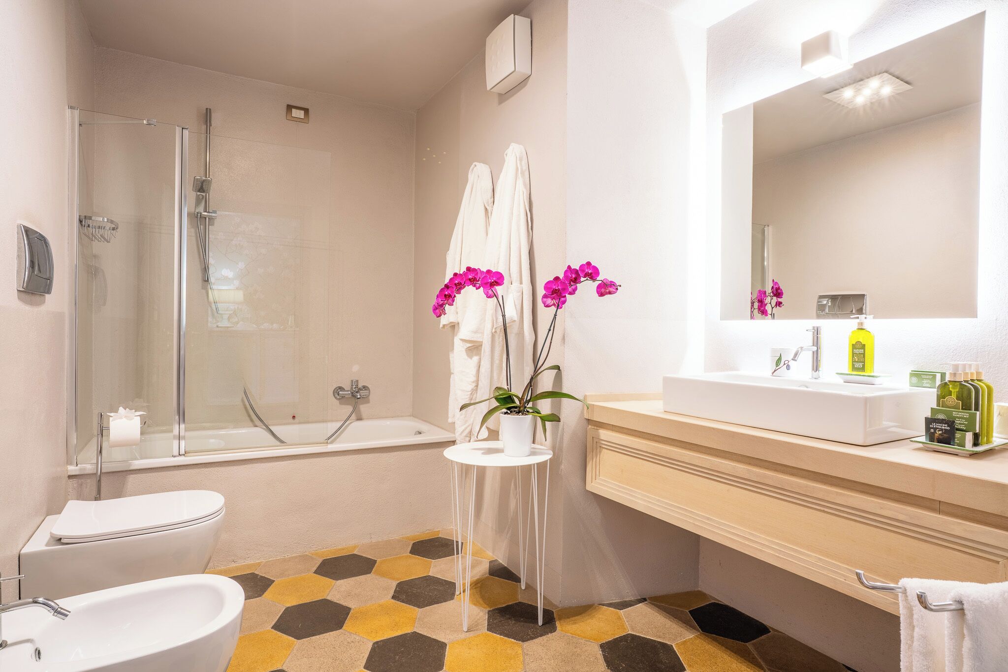 Ein modernes Badezimmer mit Duschkabine aus Glas, einem weißen Waschbecken, einer Badewanne und einem kleinen weißen Tisch mit einem Topf-Orchideen.
