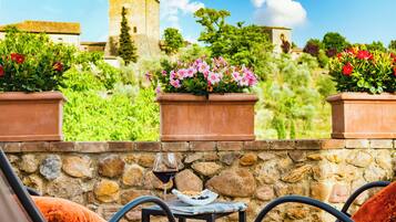 A stone wall with potted plants, a glass of red wine, and a newspaper on a small table.