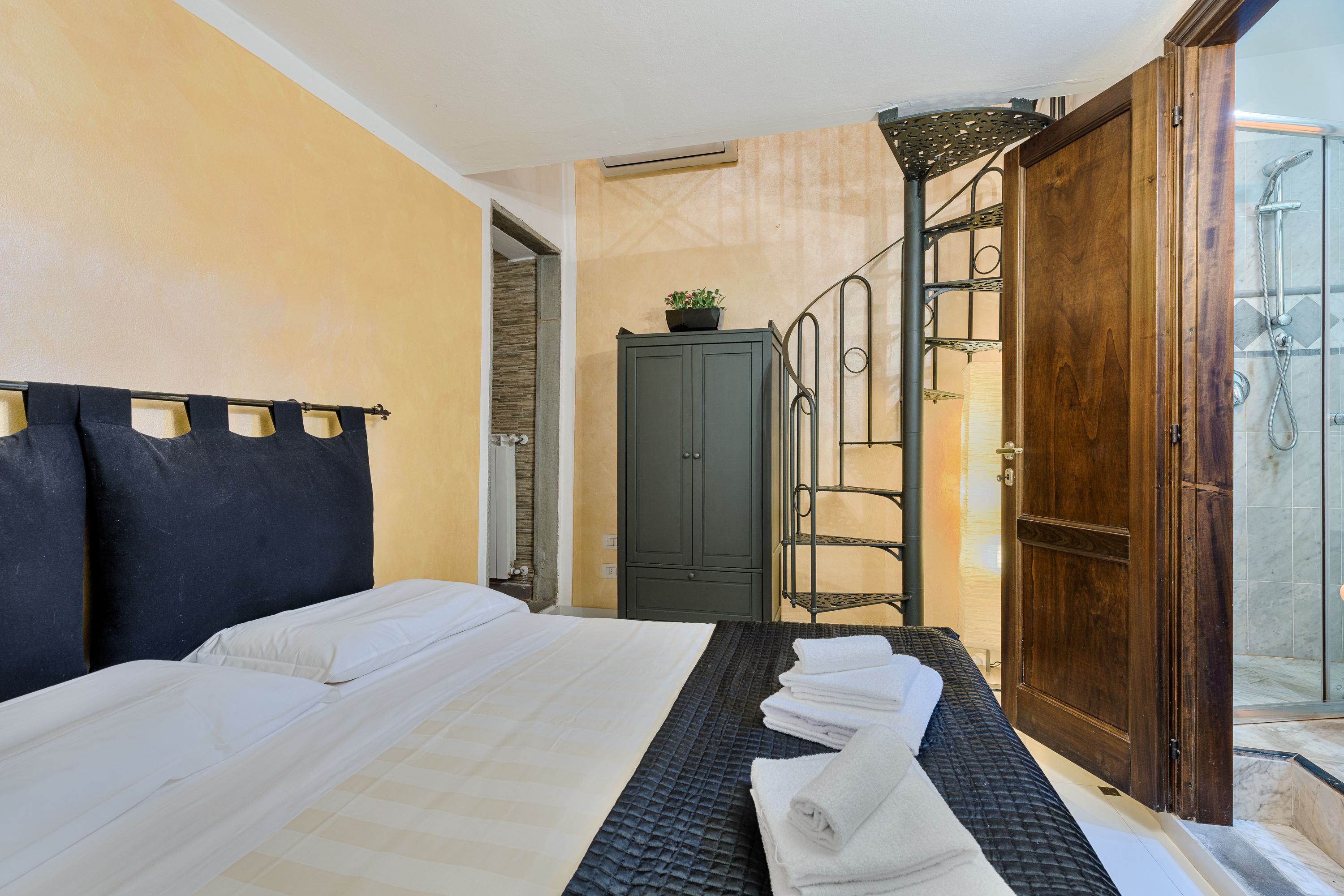 A hotel room with a bed, a wardrobe, a shower area, and a staircase.