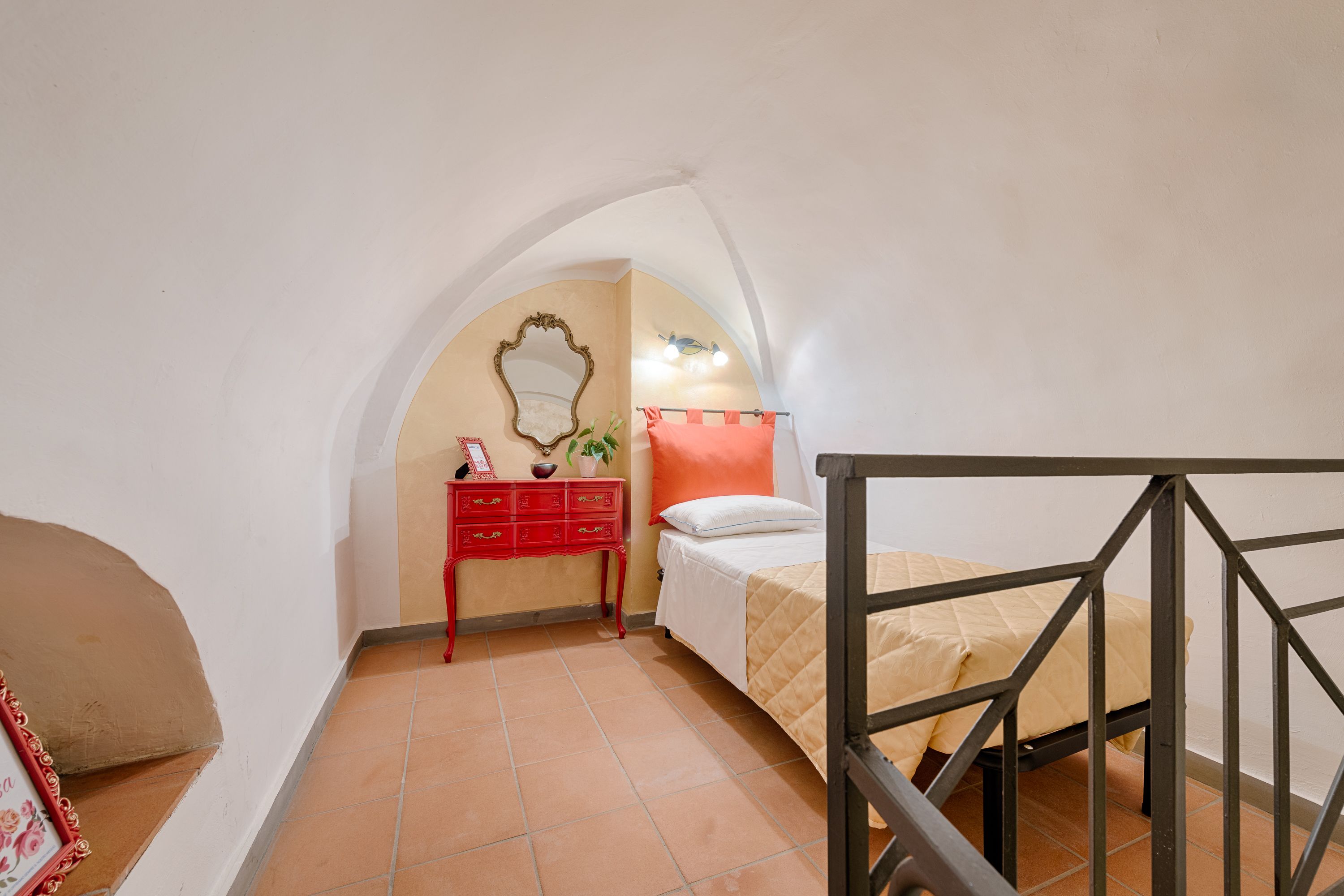 A bedroom with a bed, a red dresser, a mirror, and a staircase.