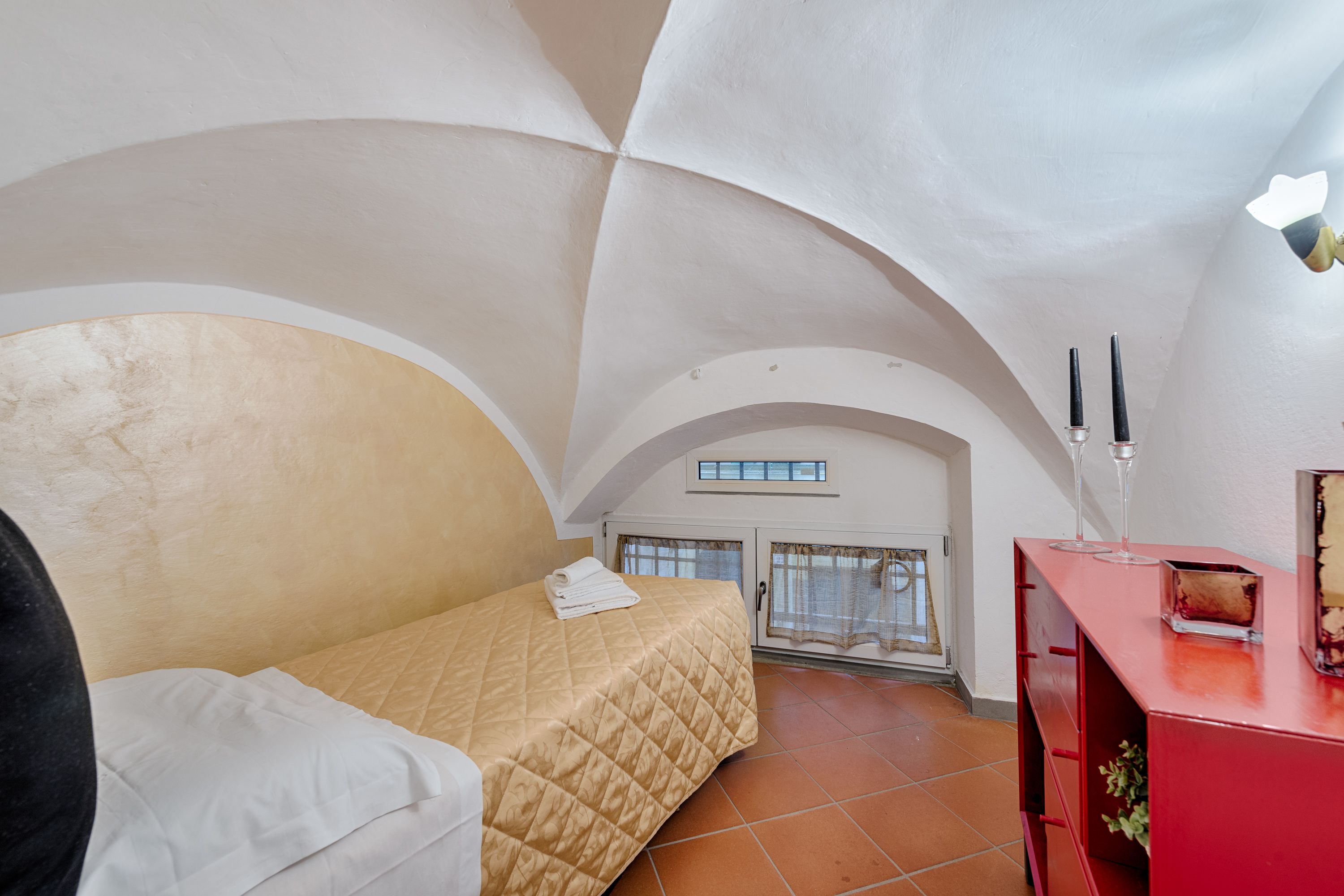 Un dormitorio con cama, cómoda roja y ventana con cortinas.
