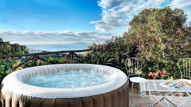 Ein Whirlpool in einem Garten mit Blick auf das Meer und einem Tisch mit Getränken und einem Buch.