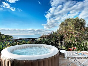 A hot tub in a garden with a view of the sea and a table with drinks and a book. - Casa Turiello (Massa Lubrense)