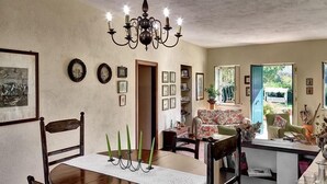 Ein Essbereich mit einer Chandelüster, Holzsesseln, einem Tisch mit weißem Tischtuch und gerahmten Bildern an der Wand.