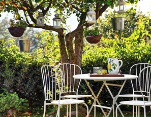 A garden table with white metal chairs, surrounded by lush greenery and hanging lanterns. - Casa Turiello (Massa Lubrense)