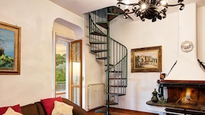 Una sala de estar acogedora con un sofá marrón, una chimenea, una escalera en espiral y una mesa de comedor con una bandeja.