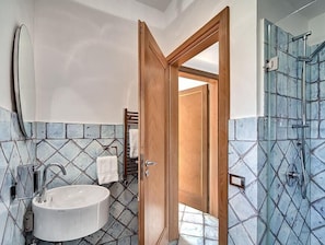 Casa de banho com lavatório branco, porta de madeira e área de duche com azulejos de mosaico azul.