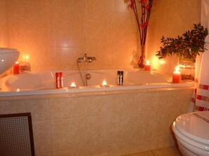 Un baño con una bañera, dos velas y un florero con flores.