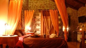Una habitación acogedora con cama, cortinas, una mesa con velas y un televisor en la pared.