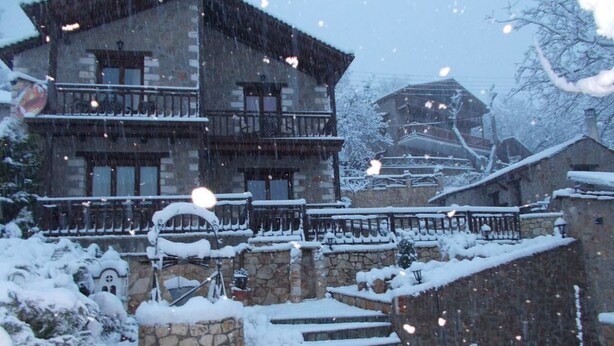 Un edificio de piedra con un balcón, rodeado de escalones y árboles cubiertos de nieve.