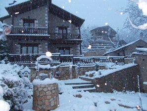 Un edificio de piedra con un balcón, rodeado de escalones y árboles cubiertos de nieve.