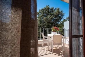 Un balcon avec une table et des chaises blanches, un pot de fleurs avec des fleurs rouges et une rambarde en métal.