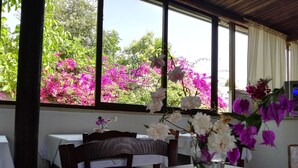 A dining area with a table set for two, a vase with flowers, and a window with a view of pink flowers outside. - Residence Missipezza (Otranto)