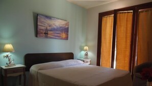 A hotel room with a bed, two bedside tables with lamps, a painting of a sunset, and a window with curtains. - Residence Missipezza (Otranto)