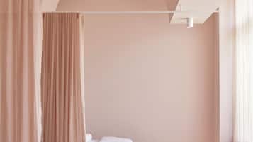 Simple, serene retreat with a single bed and two stools, set against a light-colored backdrop.