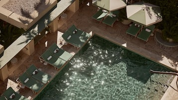 Un área de piscina con múltiples tumbonas y sombrillas, rodeada de suelo de piedra y vegetación.