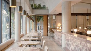 A modern restaurant with round tables, hanging pendant lights, and a bar area with stools. - The Calile Hotel (Fortitude Valley)