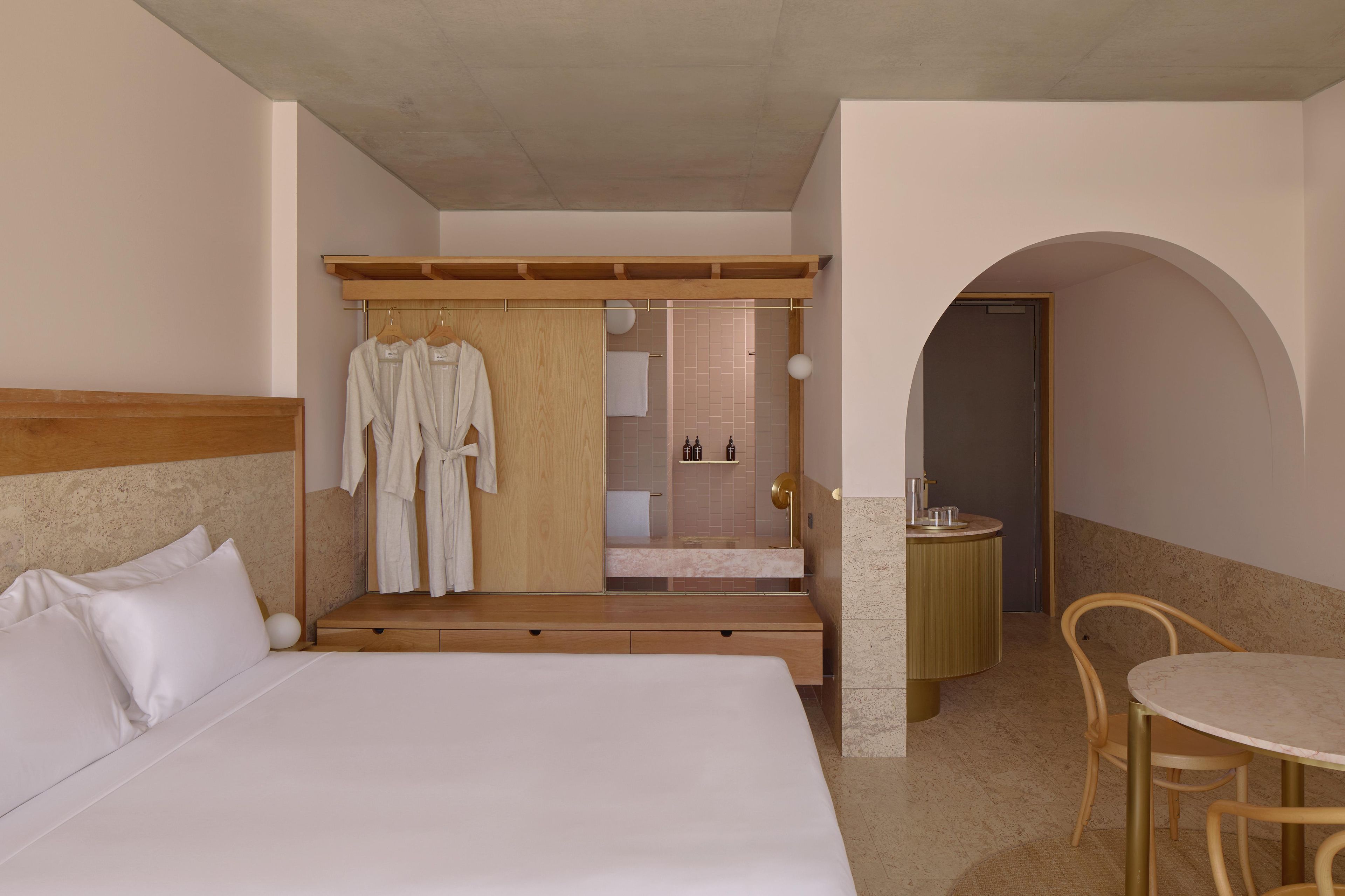 Habitación de hotel con una cama grande, un armario de madera, un baño con espejo y una zona de comedor con mesa y sillas.