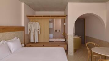 A hotel room with a large bed, a wooden wardrobe, a bathroom with a mirror, and a dining area with a table and chairs.