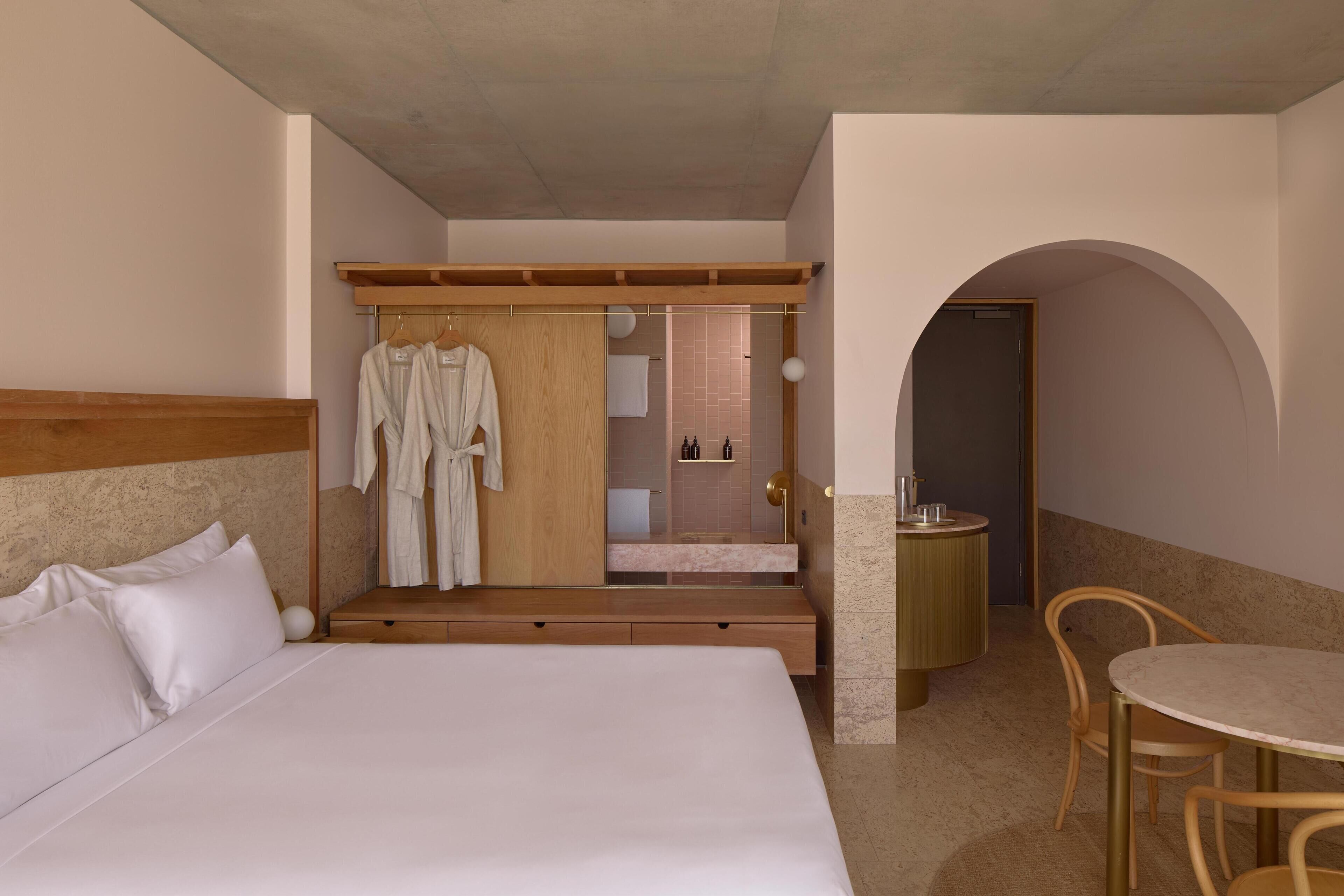 A hotel room with a large bed, a wooden headboard, a seating area with a table and chairs, and a bathroom visible through an archway.