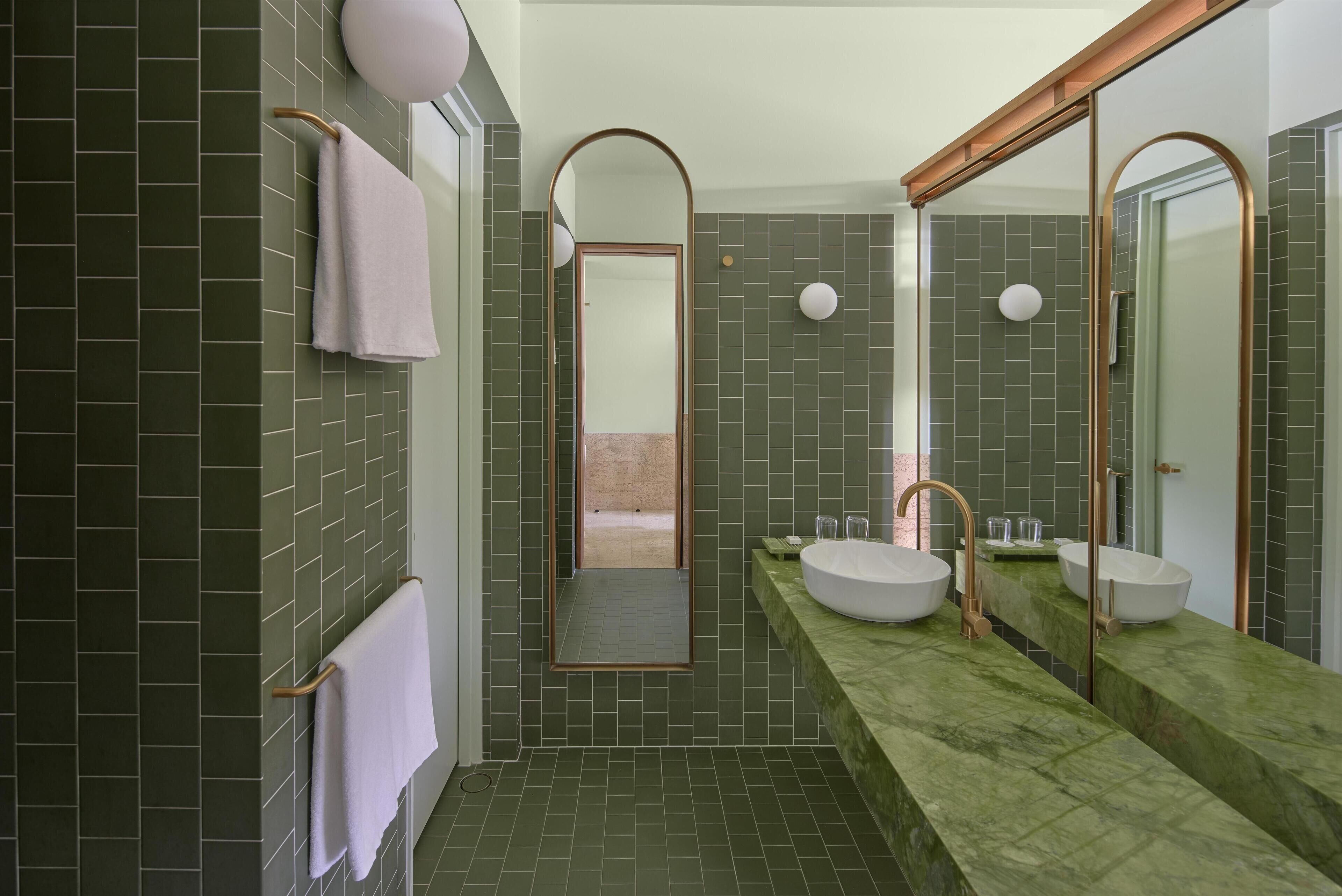 A modern bathroom with green tiles, two sinks, and a large mirror.