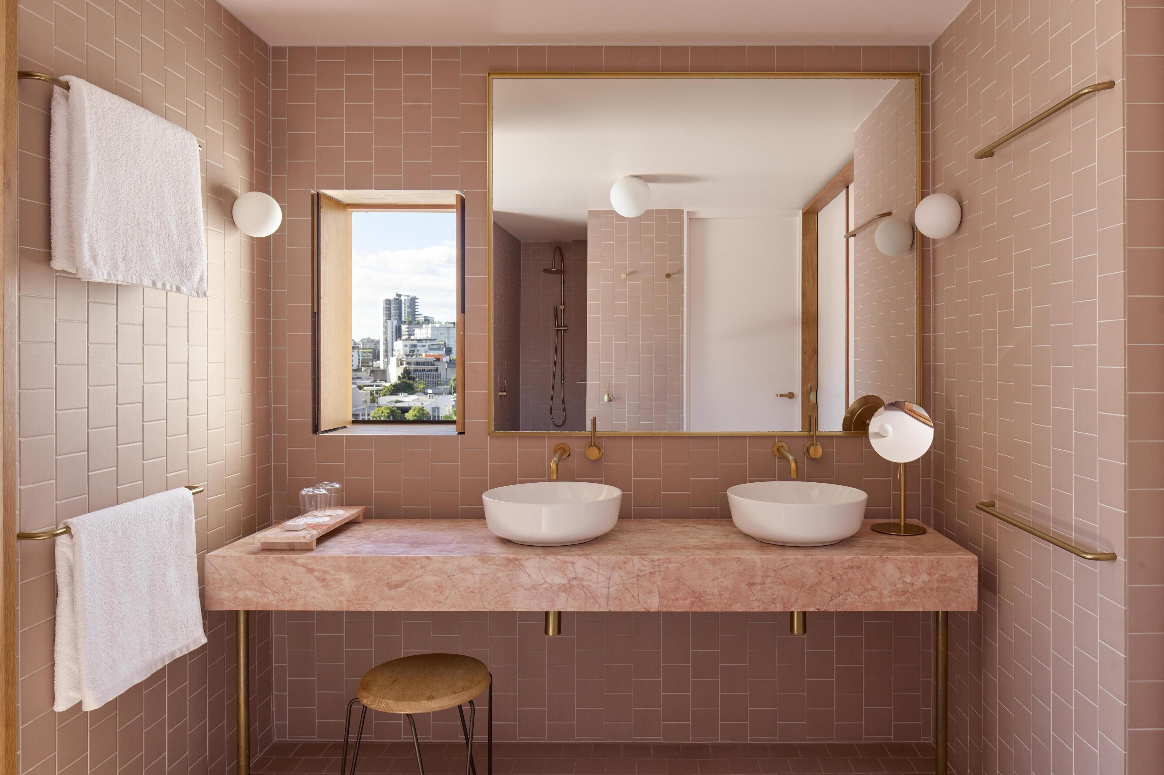 Un baño moderno con dos lavamanos, un espejo grande y vistas de la ciudad a través de una ventana.