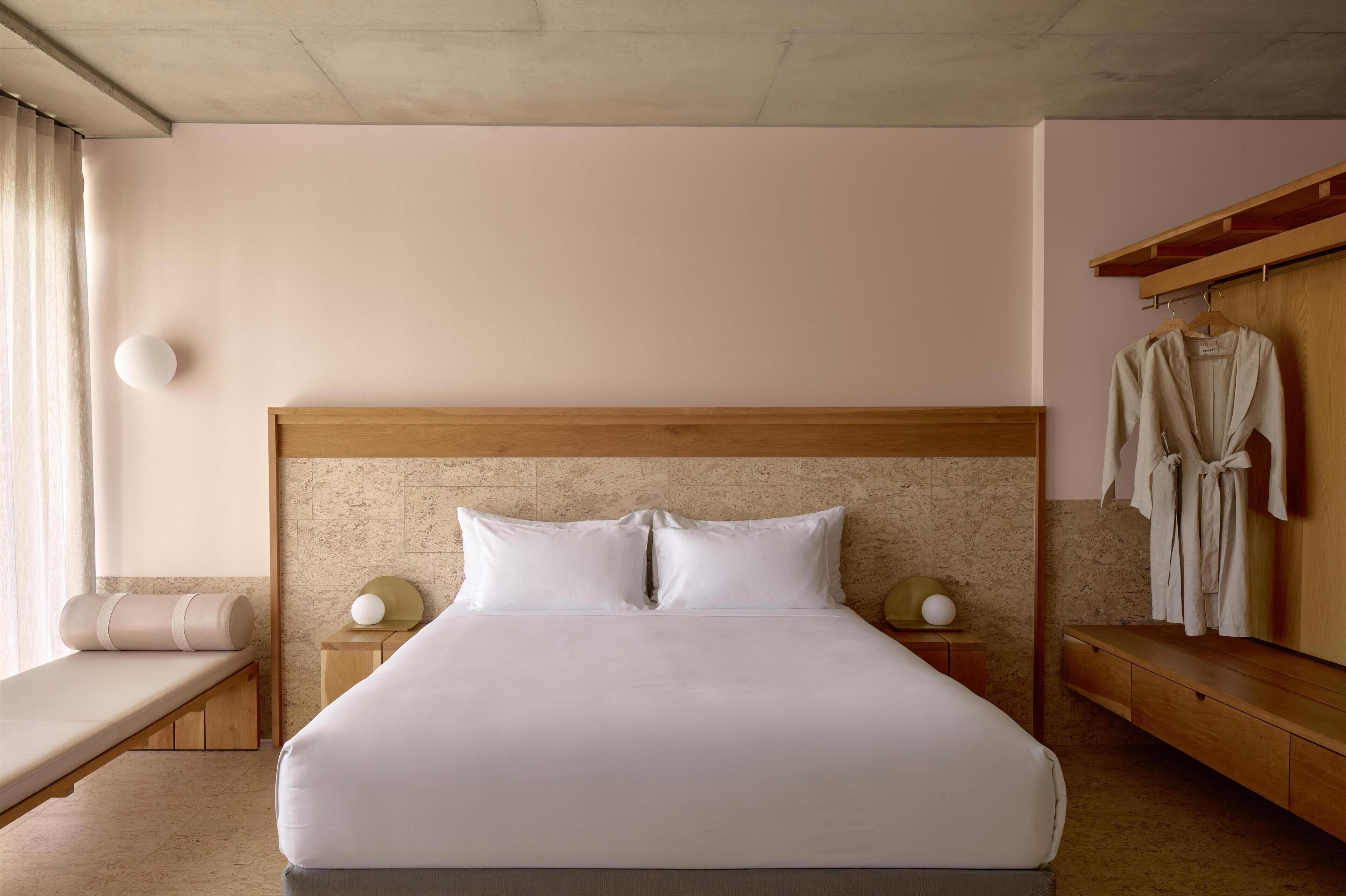 Une chambre d’hôtel bien aménagée, avec un grand lit, des tables de chevet, un banc et un porte-peignoir.