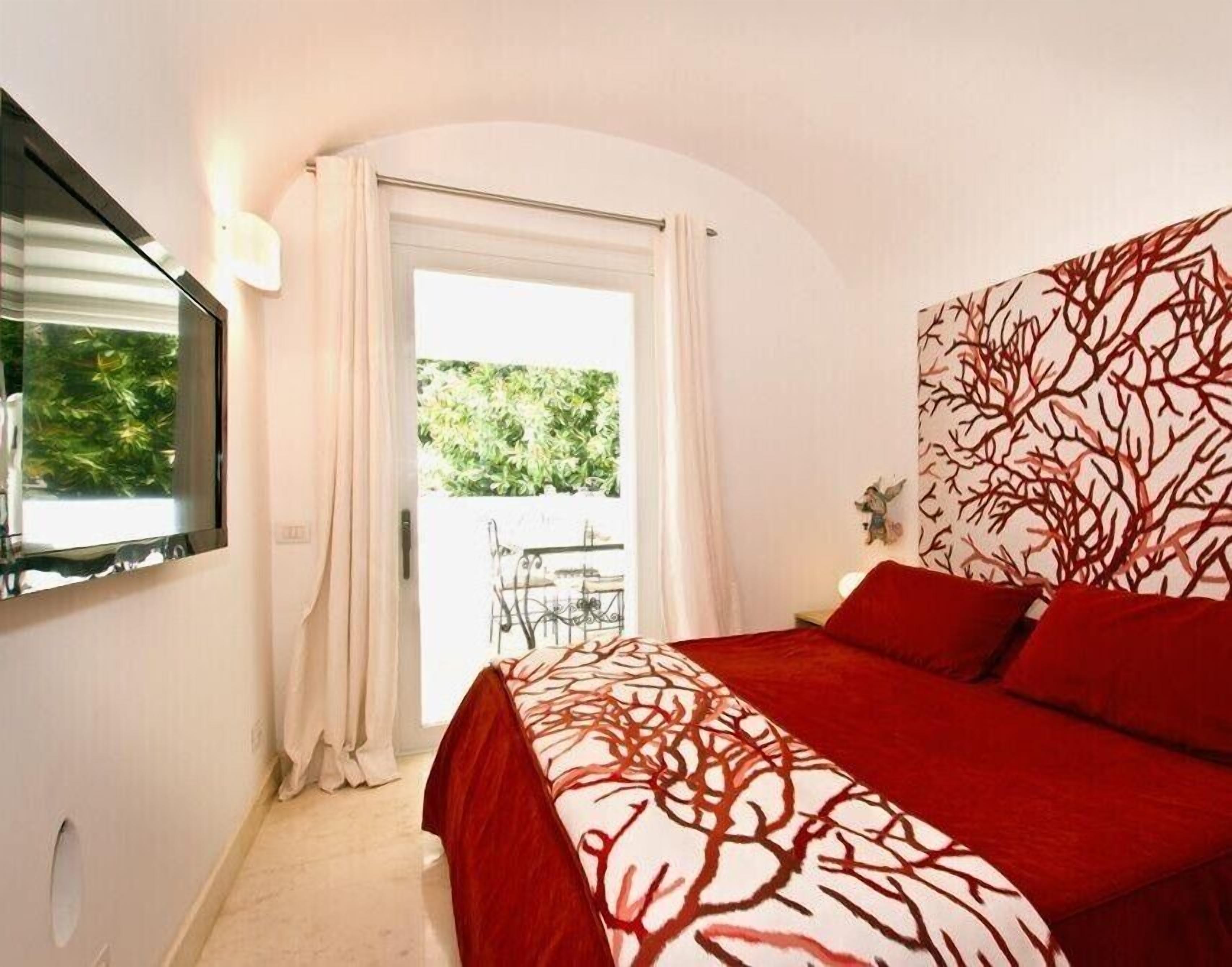 A bedroom with a bed, a TV, a window with curtains, and a view of greenery outside.