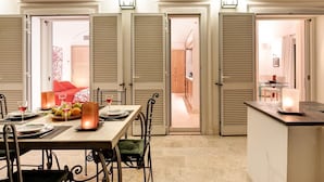 A dining area with a table set for two, a candle on the sideboard, and a view into the adjacent room through a door with shutters. - Villa Bougainvillea (Capri)