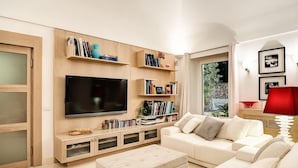 A modern living room with a large flat-screen TV, built-in bookshelves, a white sofa, and a red lamp. - Villa Bougainvillea (Capri)