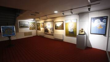 Una galería con obras expuestas, piso cubierto de alfombra roja y pared blanca.