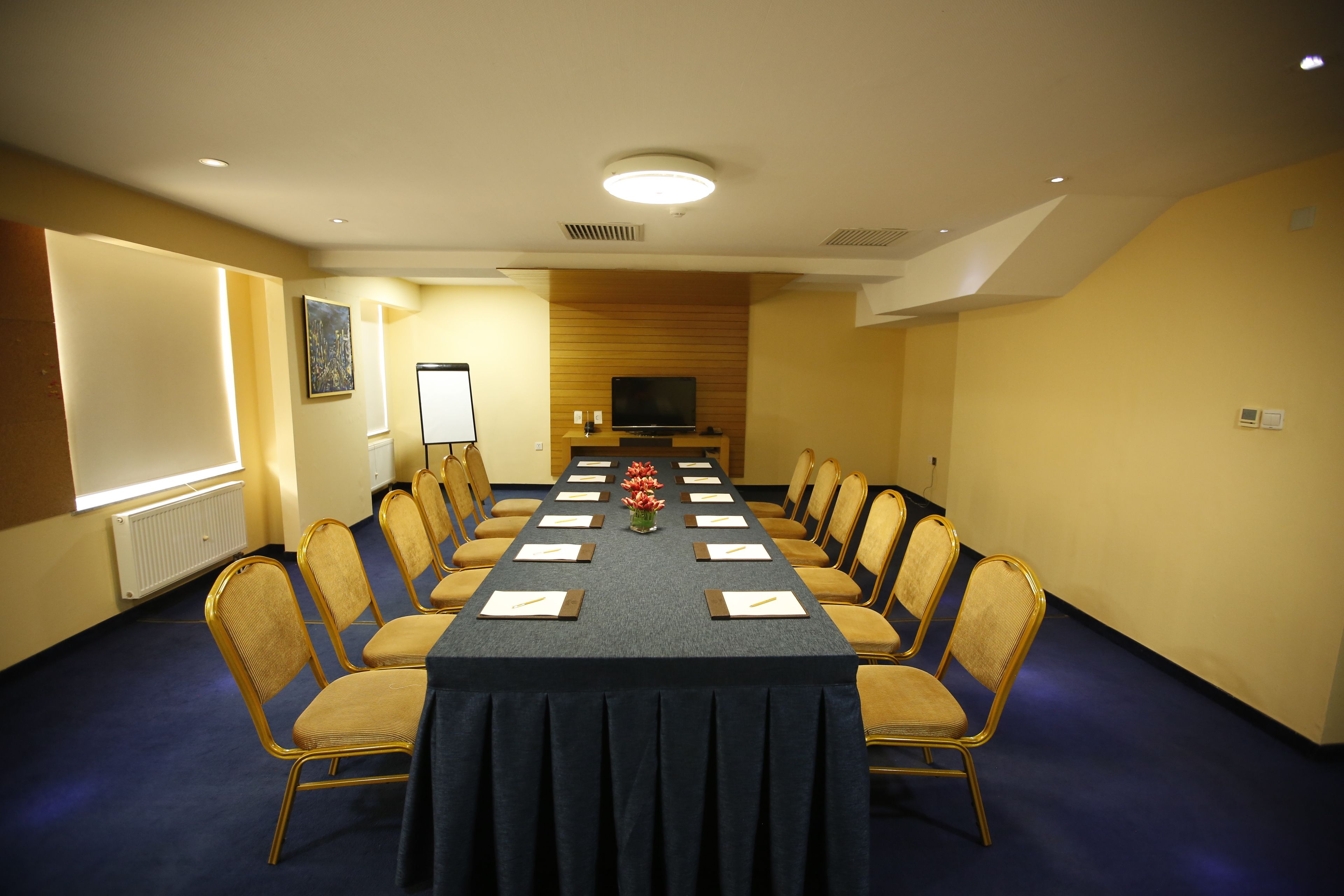 A conference room with a long table, chairs, a projector screen, and a television.