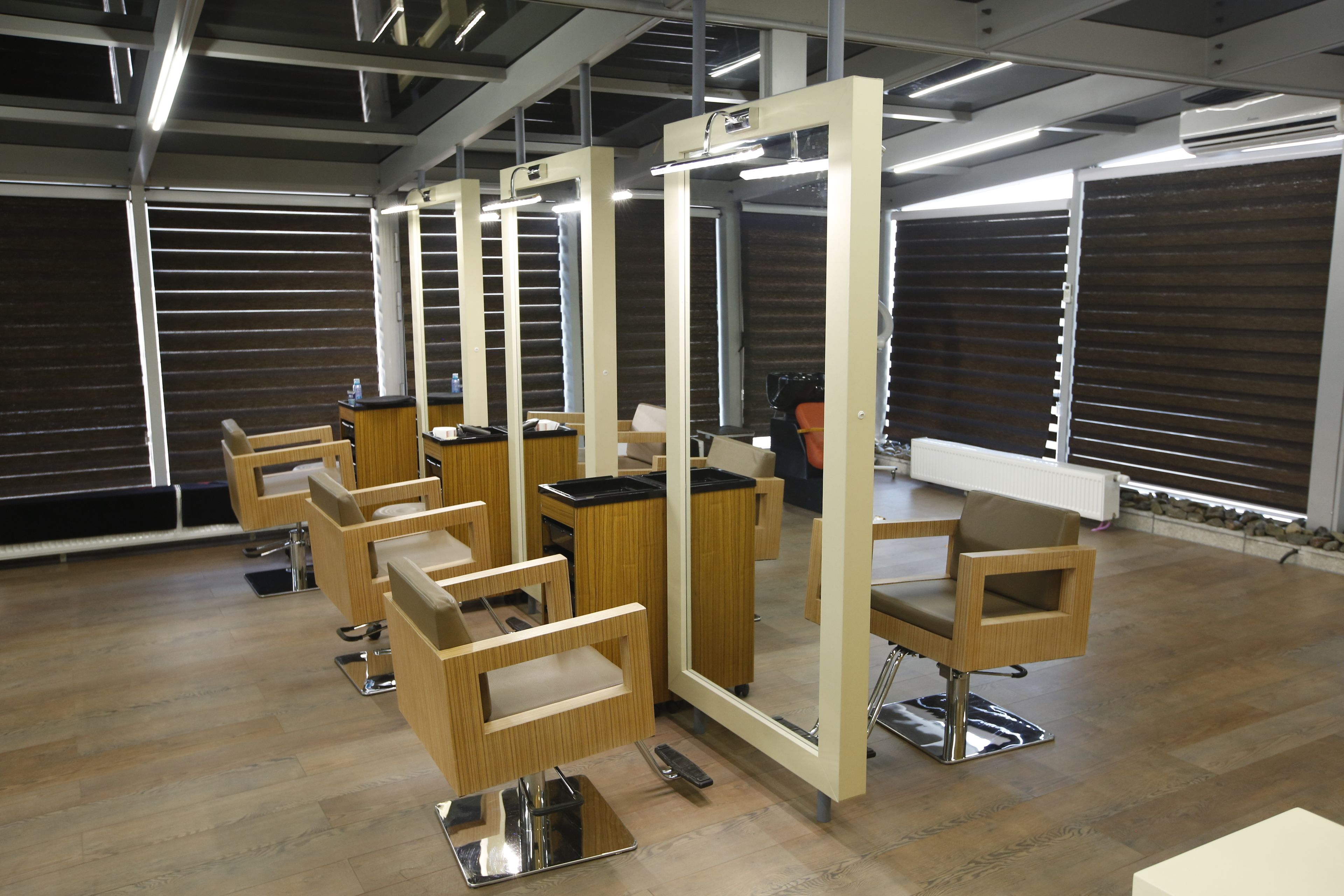 Un salón moderno con varias estaciones de peluquería, cada una con un sillón, espejo y mostrador.