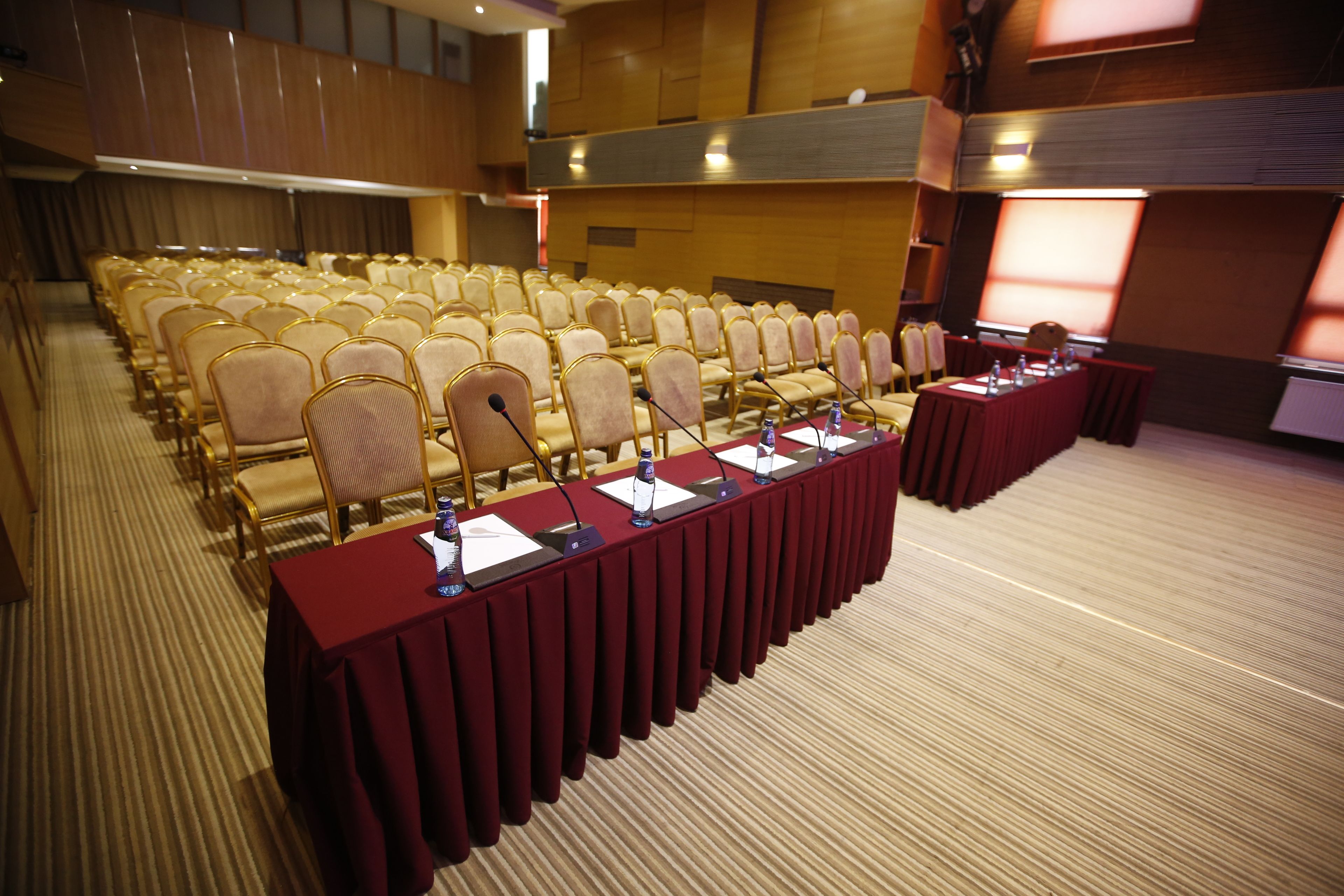 A conference room with rows of chairs, a long table with microphones, and a projection screen.